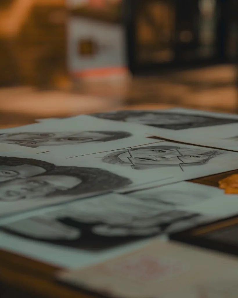 Varias láminas con dibujos a grafito apoyadas unas sobre otras en una mesa de taller